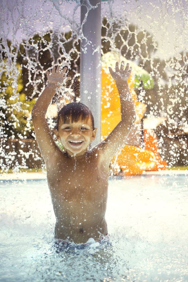 Happy boy playing with the water fountain in the pool stock photo Happy boy playing with the water fountain in the pool stock photo