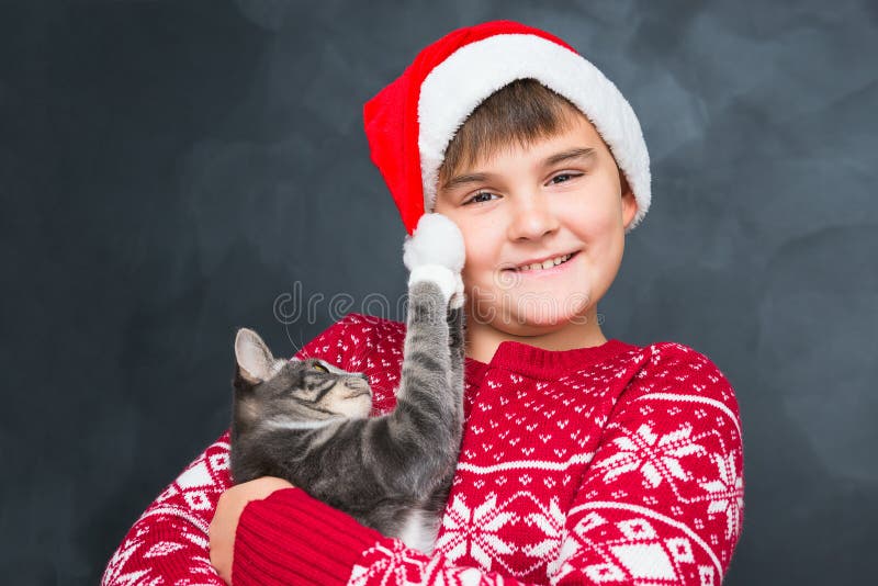 Happy boy in red New Year`s cap with gray kitten in his hands on royalty free stock image Happy boy in red New Year`s cap with gray kitten in his hands on royalty free stock image