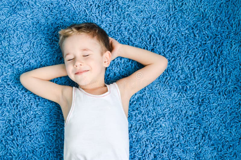 Felice ragazzo ragazzo sorridente con gli occhi chiusi sul blue carpet nel salotto di casa.