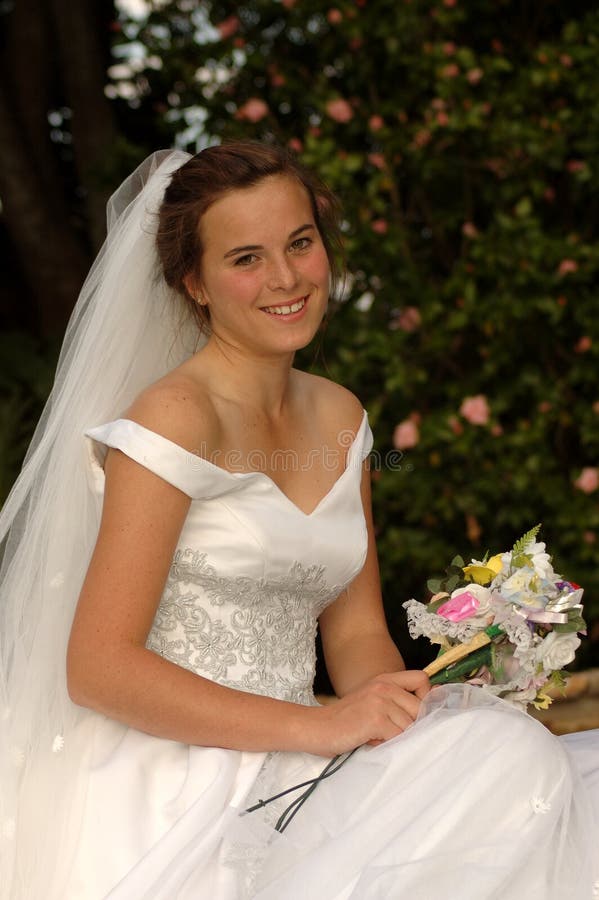Hermoso caucásico muy joven novia feliz expresión en su lindo agotador su blanco boda ropa largo tiempo velo en jardín afuera.
