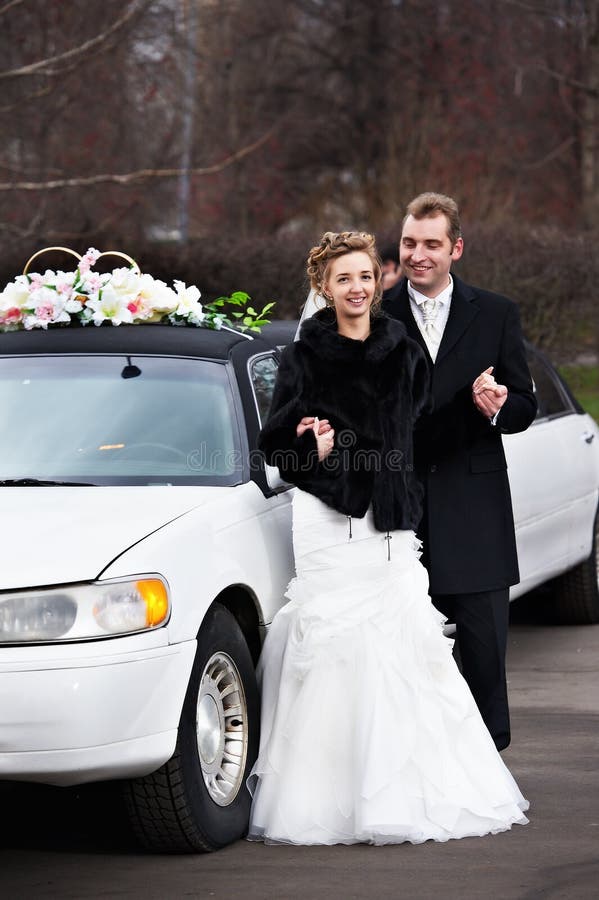 Happy bride and groom near wedding limo