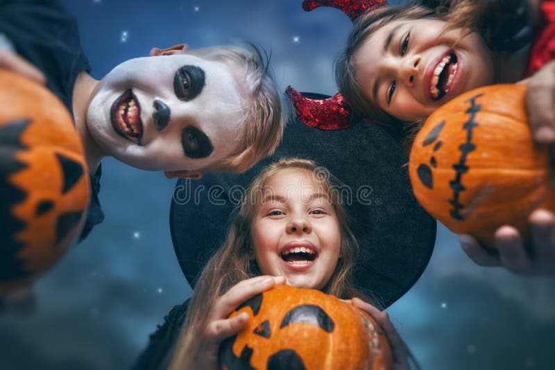 Happy brother and two sisters at Halloween. Funny kids in carnival costumes outdoors. Cheerful children and pumpkins buckets on night sky background. Happy brother and two sisters at Halloween. Funny kids in carnival costumes outdoors. Cheerful children and pumpkins buckets on night sky background.