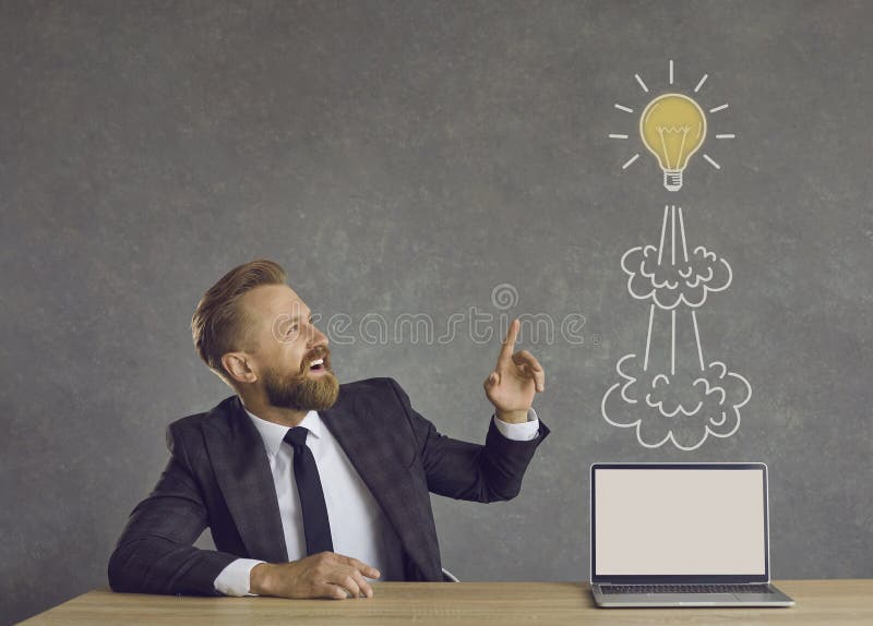 Happy businessman with laptop with mockup screen pointing at flying idea light bulb rocket royalty free stock image