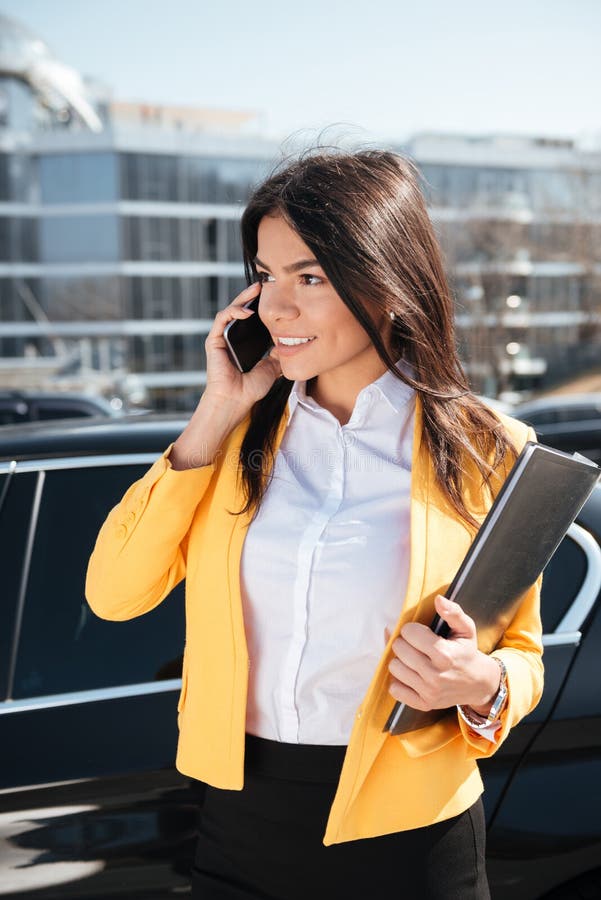 Happy businesswoman holding folder and talking on mobile phone outdoors