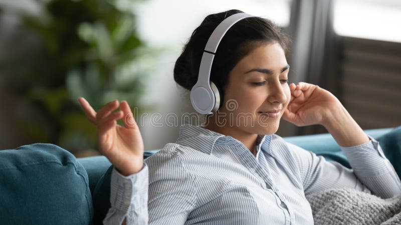 Indian girl wearing wireless headphones enjoying listening music at home