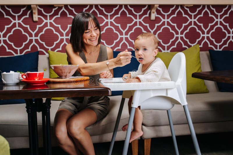 Caring mother in a cafe feeding her baby, sitting in a high chair