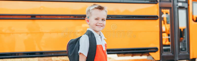 Happy Caucasian boy student with backpack near yellow bus on first September day. Education and back to school in autumn fall.