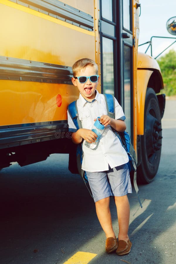 Happy Caucasian boy student kid with backpack and water bottle near yellow bus on 1 September day.