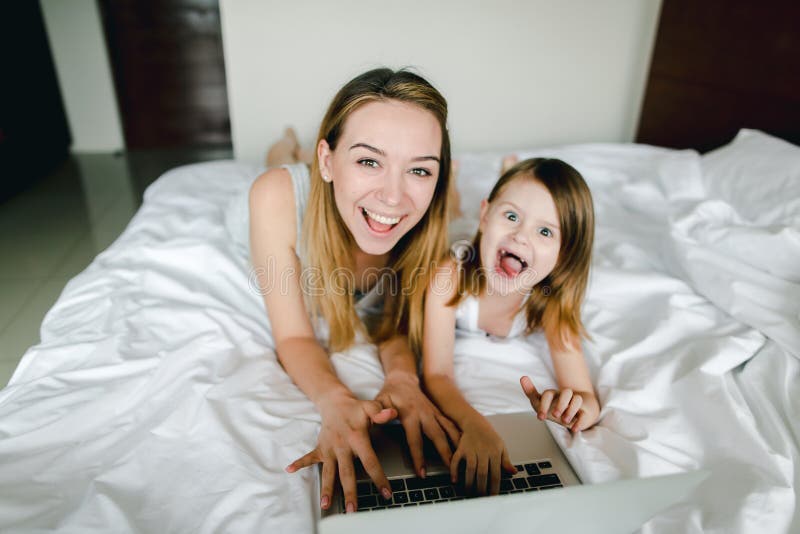 Happy caucasian female person using laptop with little daughter and lying in bed. royalty free stock photo