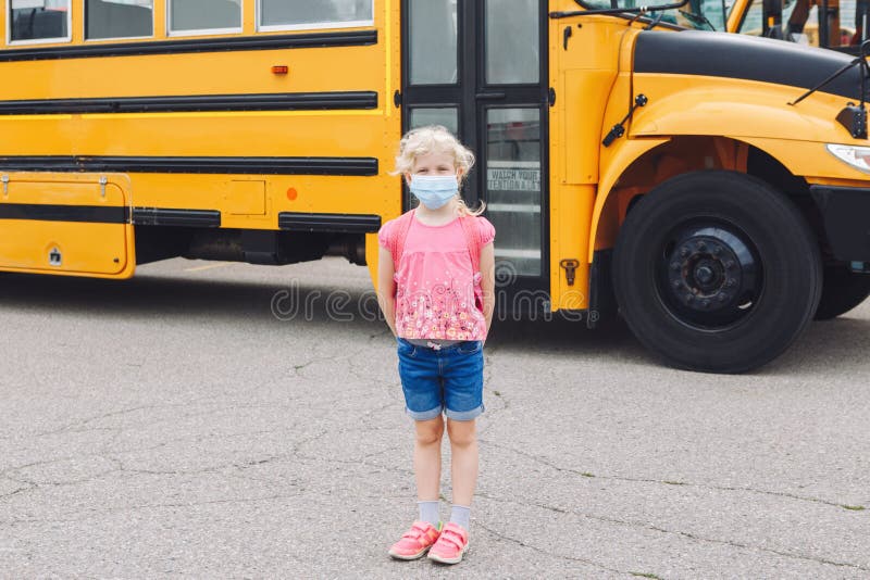 Happy Caucasian girl student wearing face mask near yellow bus. Kid with personal protective equipment on face. Education and back stock photo Happy Caucasian girl student wearing face mask near yellow bus. Kid with personal protective equipment on face. Education and back stock photo