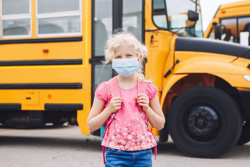 Happy Caucasian girl student wearing face mask near yellow bus. Kid with personal protective equipment on face. Education and back royalty free stock photo Happy Caucasian girl student wearing face mask near yellow bus. Kid with personal protective equipment on face. Education and back royalty free stock photo