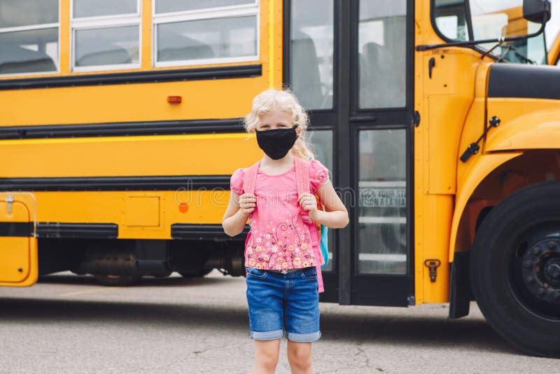 Happy Caucasian girl student wearing face mask near yellow bus. Kid with personal protective equipment on face. Education and back royalty free stock images Happy Caucasian girl student wearing face mask near yellow bus. Kid with personal protective equipment on face. Education and back royalty free stock images