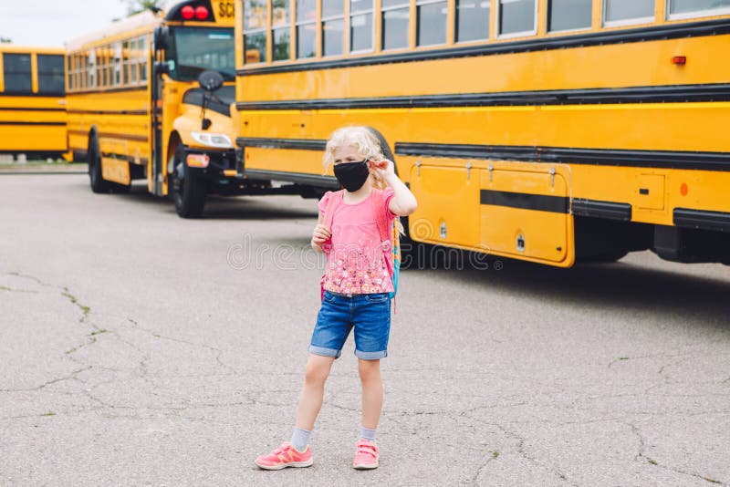 Happy Caucasian girl student wearing face mask near yellow bus. Kid with personal protective equipment on face. Education and back royalty free stock photos Happy Caucasian girl student wearing face mask near yellow bus. Kid with personal protective equipment on face. Education and back royalty free stock photos