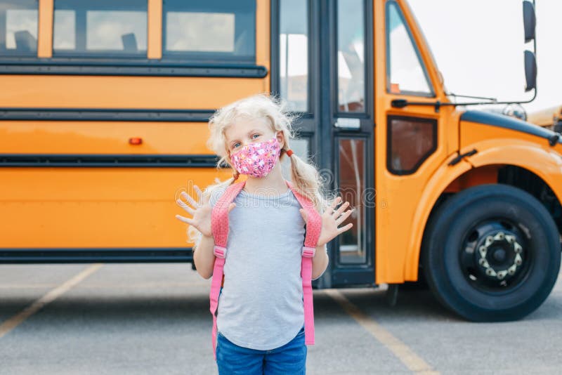 Happy Caucasian girl student wearing face mask near yellow bus. Kid with personal protective equipment on a face. Education, back stock photography Happy Caucasian girl student wearing face mask near yellow bus. Kid with personal protective equipment on a face. Education, back stock photography