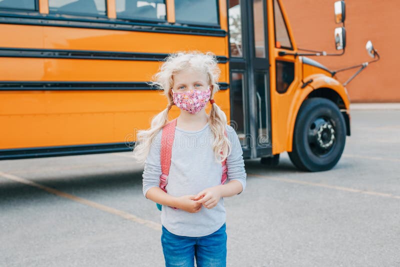 Happy Caucasian girl student wearing face mask near yellow bus. Kid with personal protective equipment on face. Education and back royalty free stock images Happy Caucasian girl student wearing face mask near yellow bus. Kid with personal protective equipment on face. Education and back royalty free stock images
