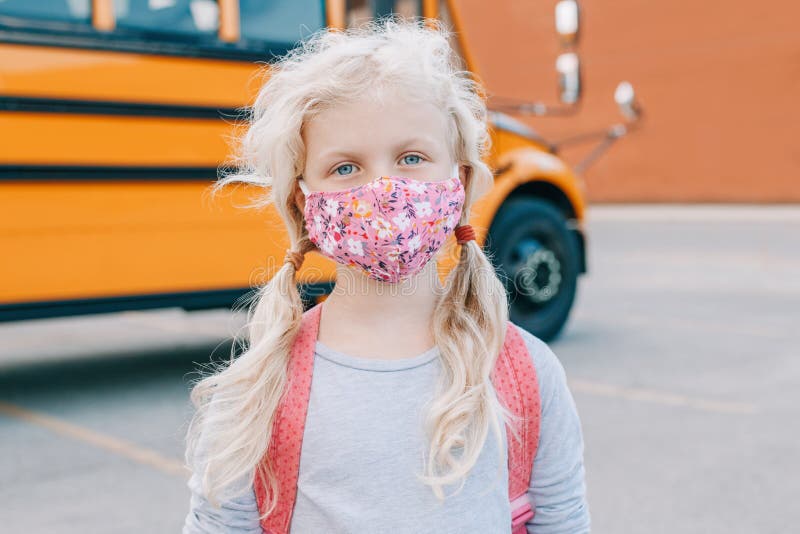 Happy Caucasian girl student wearing face mask near yellow bus. Kid with personal protective equipment on a face. Education, back royalty free stock image Happy Caucasian girl student wearing face mask near yellow bus. Kid with personal protective equipment on a face. Education, back royalty free stock image