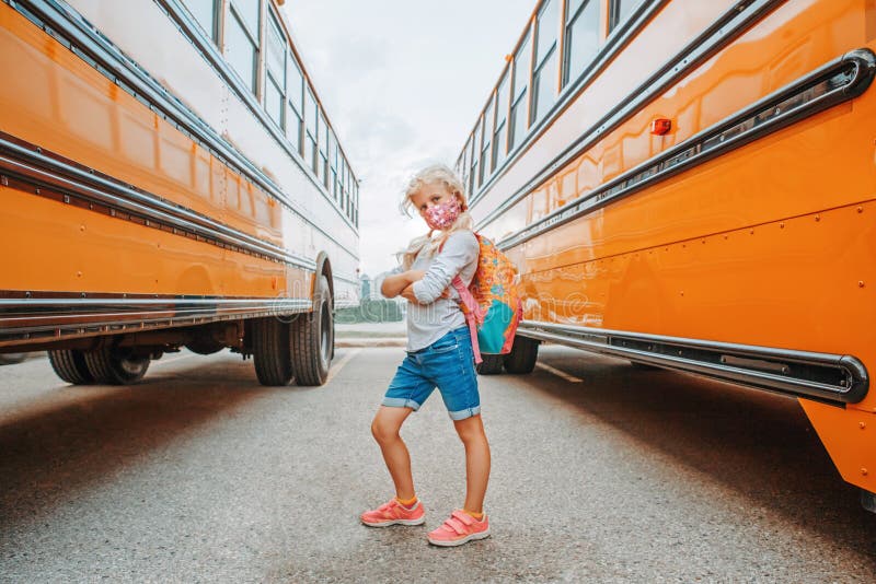 Happy Caucasian girl student wearing face mask near yellow bus. Kid with personal protective equipment on a face. Education, back stock photo Happy Caucasian girl student wearing face mask near yellow bus. Kid with personal protective equipment on a face. Education, back stock photo