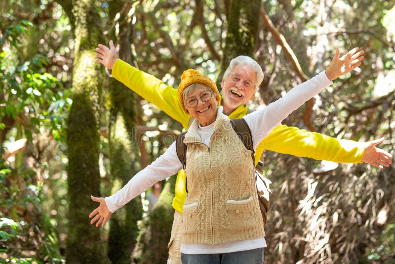 Happy Caucasian Senior Couple With Backpack Walking In The Forest Looking At Camera With