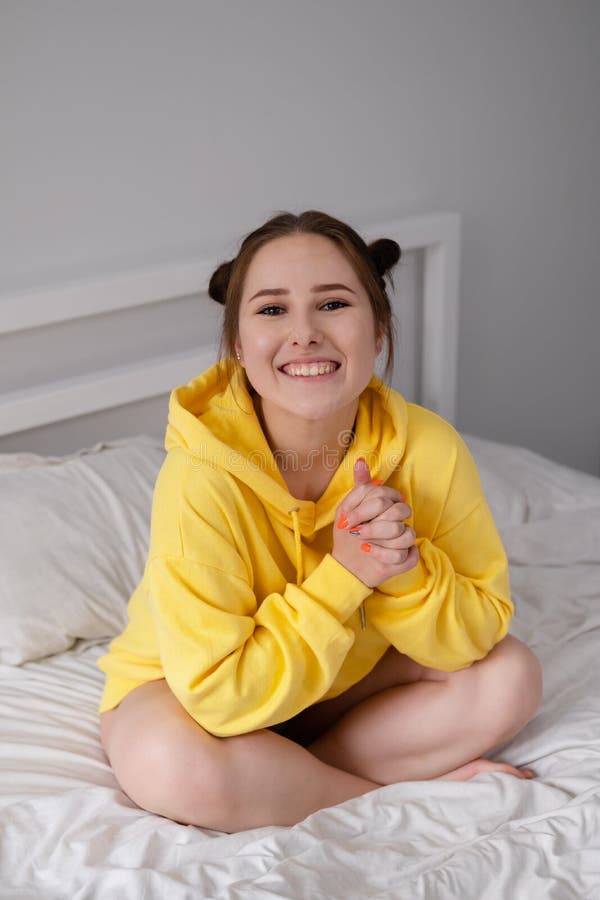 Happy Cheerful Brunette Girl In Yellow Hoodie In White Bedroom Sitting 