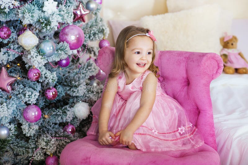 Happy cheerful little girl excited at Christmas Eve, sitting under decorated illuminated Tree. Greeting card or cover royalty free stock image Happy cheerful little girl excited at Christmas Eve, sitting under decorated illuminated Tree. Greeting card or cover royalty free stock image