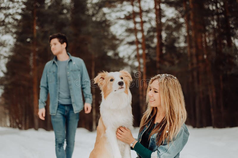 Happy cheerful smiling couple of young people in denim suits in snowy forest in winter with red dog border collie royalty free stock images Happy cheerful smiling couple of young people in denim suits in snowy forest in winter with red dog border collie royalty free stock images