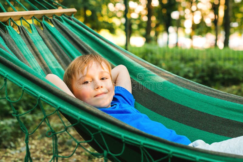 Happy child boy lying in a hammock in garden. Summer holidays concept. The child is resting in nature. Cute kid enjoy summer