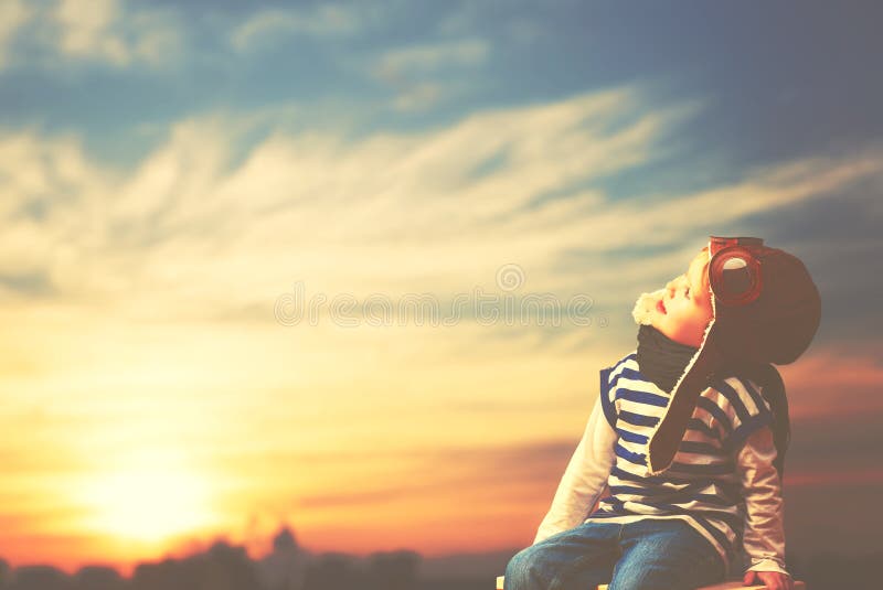 Happy child dreams of becoming pilot aviator on sky sunset background