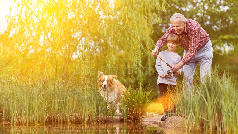 Child fishing with grandpa and dog by the lake in summer