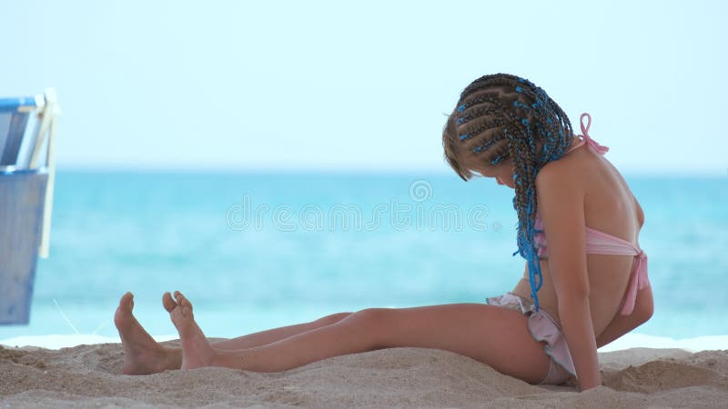 Pretty preteen girl in bikini swimsuit playing with sand in umbrella shadow  during summer tropical vacation Stock Photo