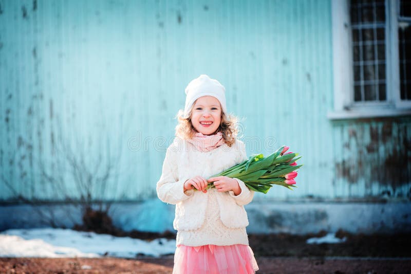 Happy child girl with bouquet of tulips having fun on the walk in early spring