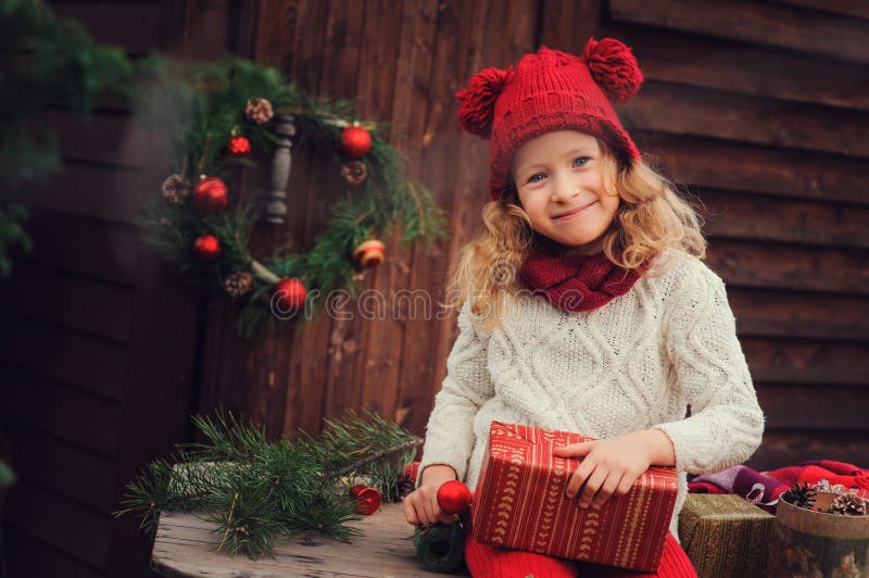 Happy child girl celebrating christmas outdoor at cozy wooden country house with gifts