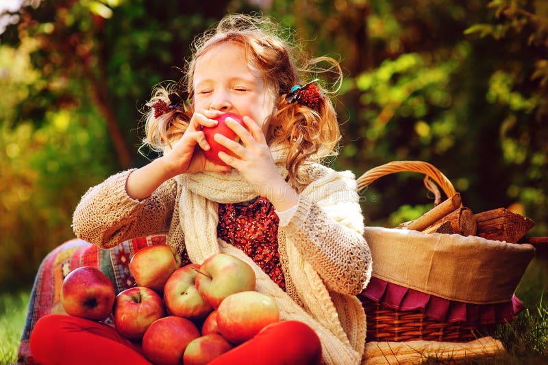 Happy child girl eating apples in autumn garden