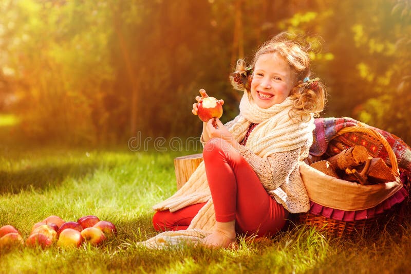 Happy child girl eating apples in autumn sunny garden