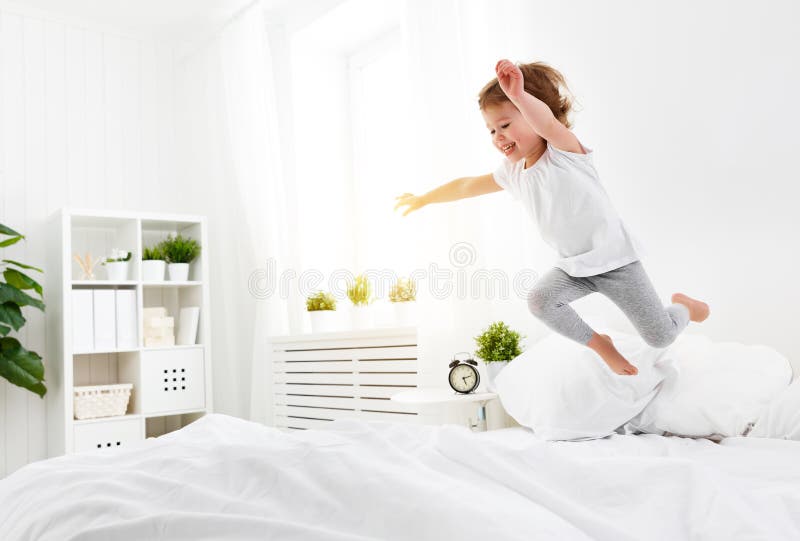 Happy child girl jumps and plays bed