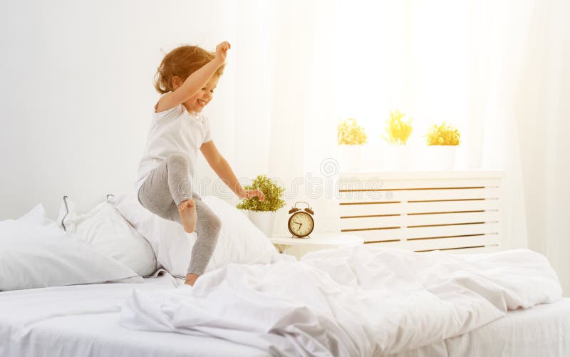 Happy child girl jumps and plays bed