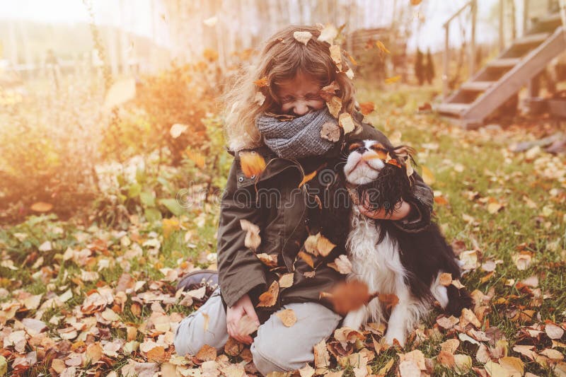 Happy child girl playing in autumn with her cavalier king charles spaniel dog