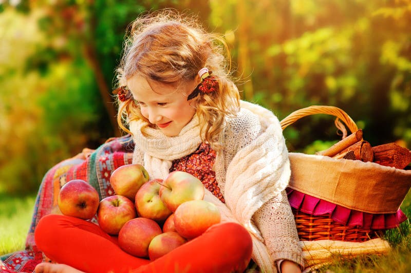 Happy child girl sitting with apples in autumn sunny garden