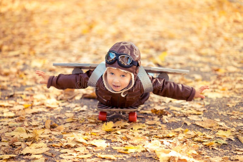 Happy child having fun outdoor in autumn park. Kid pilot playing against yellow blurred leaves background
