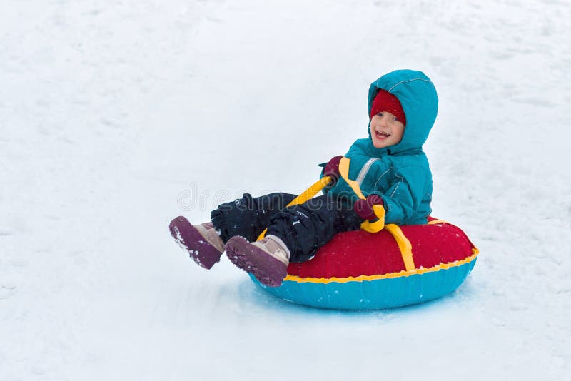 Happy child. little boy in winter ride on a sled from the mountain. Kid long and happy smiles royalty free stock image Happy child. little boy in winter ride on a sled from the mountain. Kid long and happy smiles royalty free stock image