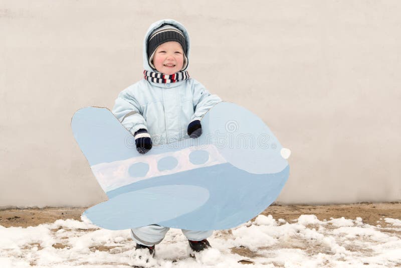 Happy child in winter fashion clothes posing with a toy airplane in the courtyard of his village house. First snow, family, tradit