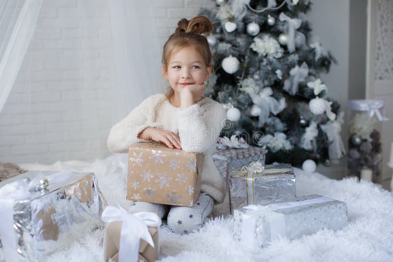 Little girl sitting on the floor near the Christmas tree with Christmas gift in hands.