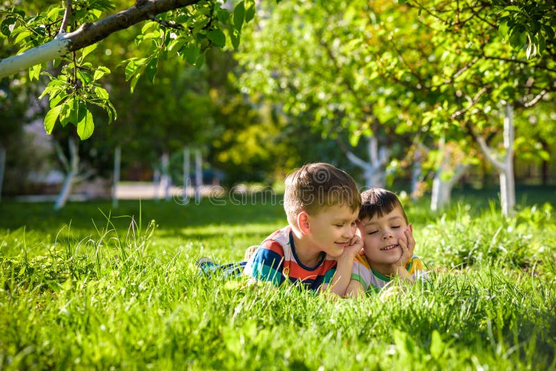 Happy children having fun outdoors. Kids playing in summer park. Little boy and his brother laying on green fresh grass holiday ca