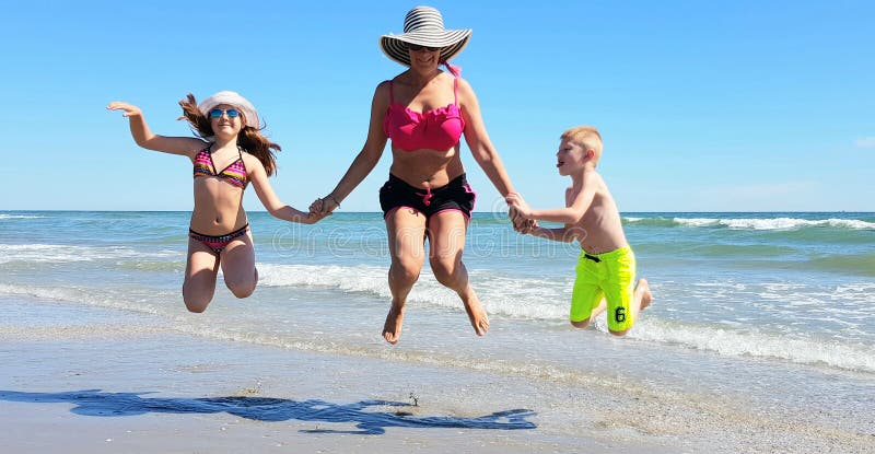 Happy children and mom jump on the beach in a sunny day of summer stock image Happy children and mom jump on the beach in a sunny day of summer stock image