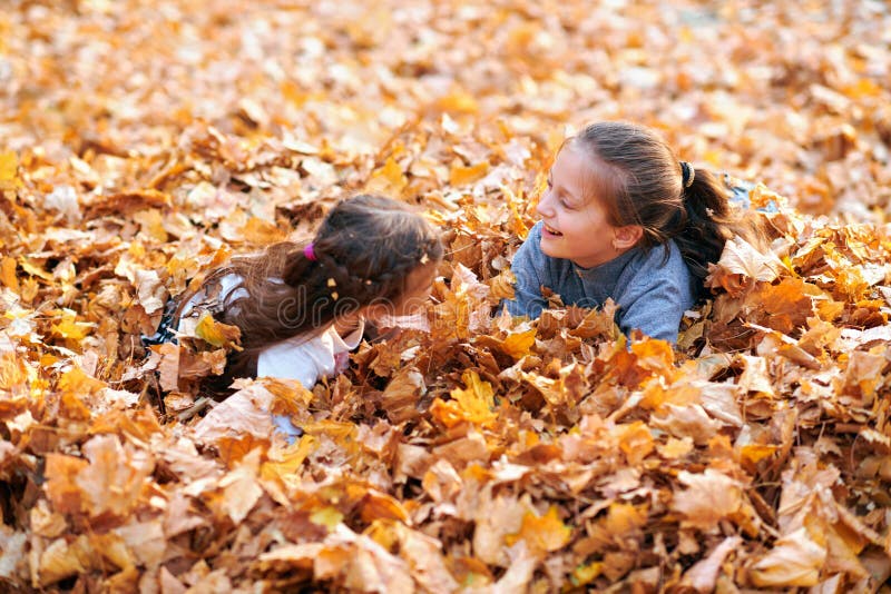 Happy children playing in heap of yellow leaves, posing, smiling and having fun in autumn city park. Bright yellow trees and stock photo Happy children playing in heap of yellow leaves, posing, smiling and having fun in autumn city park. Bright yellow trees and stock photo