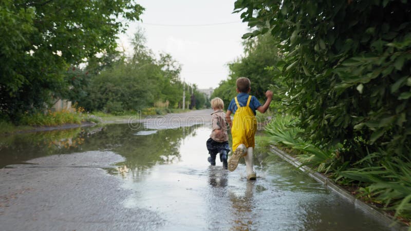 Happy children, wholesome happy brothers in rubber boots have fun together enjoying jogging in puddles after rain by