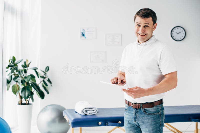 happy-chiropractor-holding-digital-tablet-hospital-looking-camera-chiropractor-holding-digital-tablet-hospital-184486219.jpg