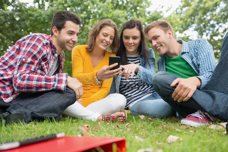 Happy college students looking at mobile phone in park stock photo Happy college students looking at mobile phone in park stock photo