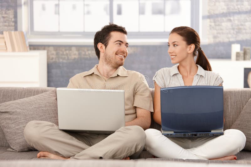 Felice, coppia, seduta sul divano a casa, navigando in internet sul separata, computer portatili, sorridere, divertirsi.