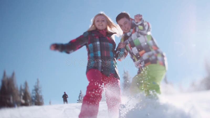 Happy couple in colorful ski costumes. Floor level shooting of joyful young people sliding in the snow towards the