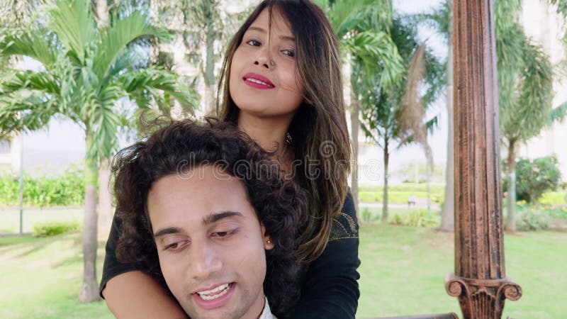 Happy couple enjoying a serene moment in a lush park with a woman embracing a man from behind both smiling contentedly